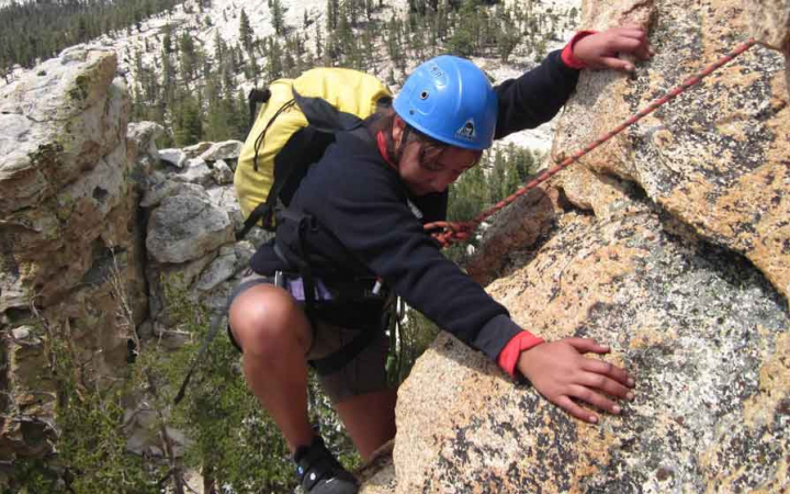 a person wearing safety gear and secured by ropes rock climbs high above the trees below
